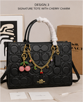 Black signature tote bag with cherry charm and Coach logo, placed on a light surface with a neutral background.