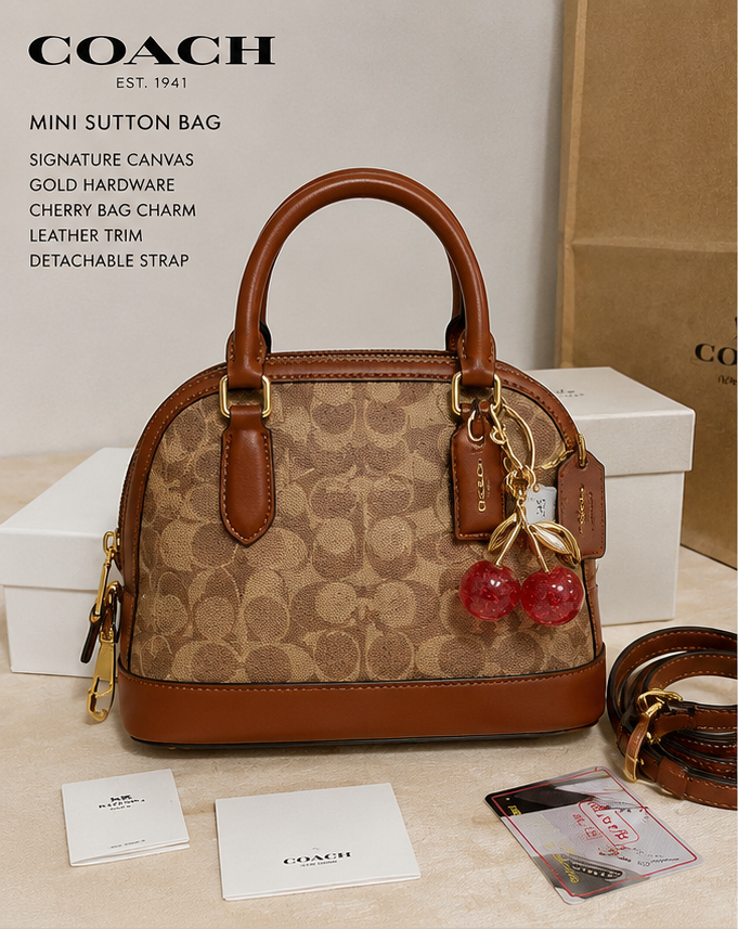 Coach Mini Sutton bag with cherry charm on a beige surface with packaging in the background.